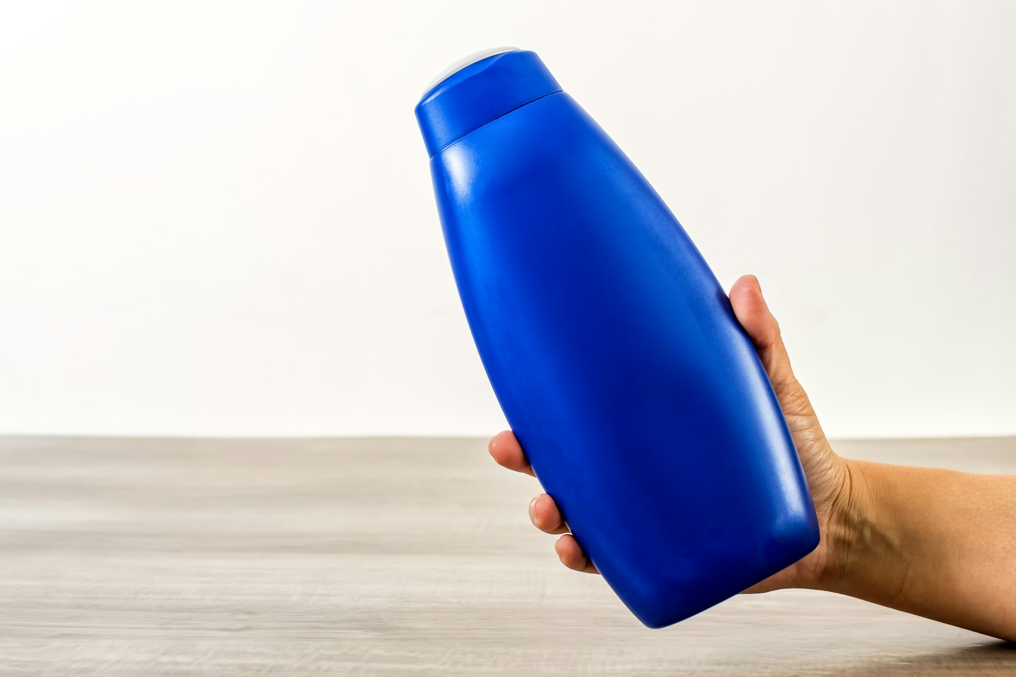 Female hand holding an empty blueplastic shampoo bottle